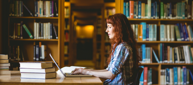 Kobieta siedząca w bibliotece, która korzysta z laptopa. 